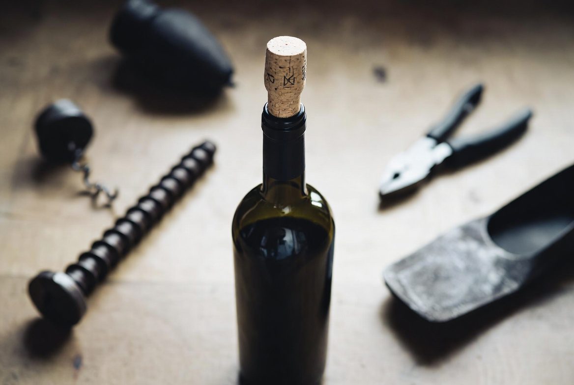 Abrir Vinho Sem Saca Rolha: Mesa com garrafa de vinho, parafuso e alicate, representando o método de emergência.