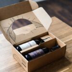 Assinatura de Vinhos: caixa de clube de vinho sendo aberta com garrafas e ficha técnica de degustação.