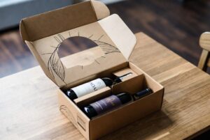 Assinatura de Vinhos: caixa de clube de vinho sendo aberta com garrafas e ficha técnica de degustação.