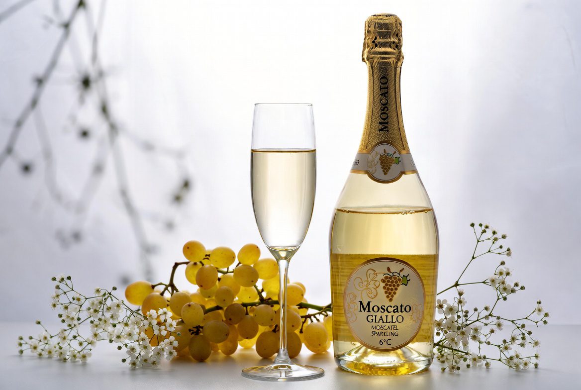 Espumante Moscatel: Garrafa gelada com taça e uvas Moscato, destacando o frescor e a doçura.