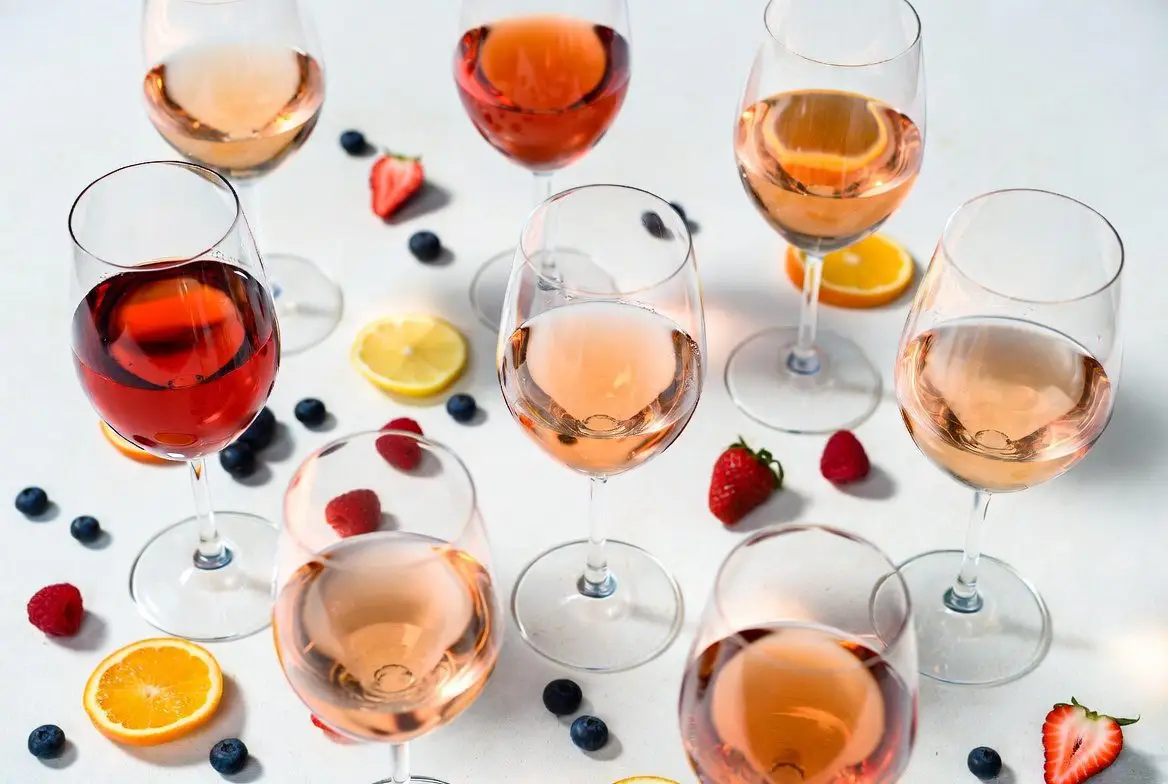 Vinho Rosé Seco: mesa com taças de rosé de diferentes tons, frutas e elementos de frescor.
