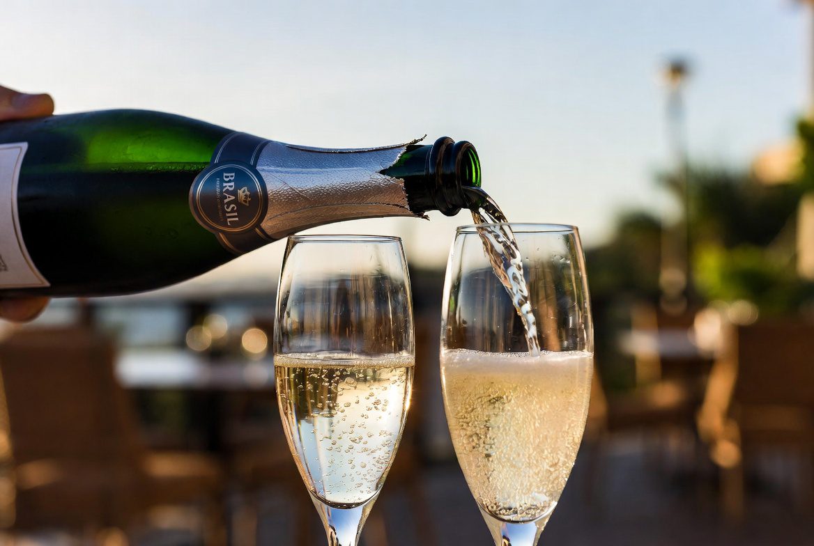 Espumantes: Garrafa de brut nacional sendo servida em taças de cristal durante o pôr do sol.
