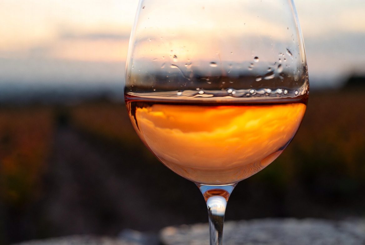 Vinho Laranja: A quarta cor do vinho em destaque em uma taça de cristal ao entardecer.