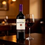 Uma garrafa de vinho chileno Reservado Concha y Toro ao lado de uma taça cheia em uma mesa de jantar.