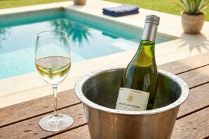 Vinho Sauvignon Blanc Chileno: Por que Ele Vale Tanto a Pena? 13 Garrafa de vinho branco Sauvignon Blanc chileno em um balde de gelo na beira da piscina em um dia ensolarado.