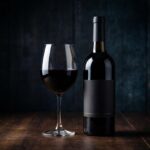 Uma garrafa de vinho Tannat uruguaio ao lado de uma taça com vinho tinto de cor muito escura e intensa.