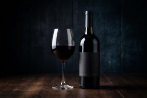 Uma garrafa de vinho Tannat uruguaio ao lado de uma taça com vinho tinto de cor muito escura e intensa.